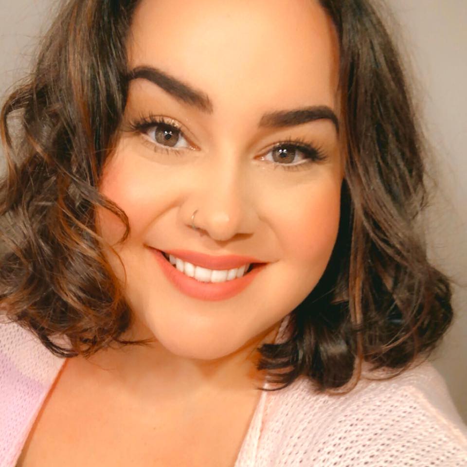 Whitney McDonald, a white woman with short brown hair, smiles broadly. Whitney wears a light cardigan and also has a nose ring.